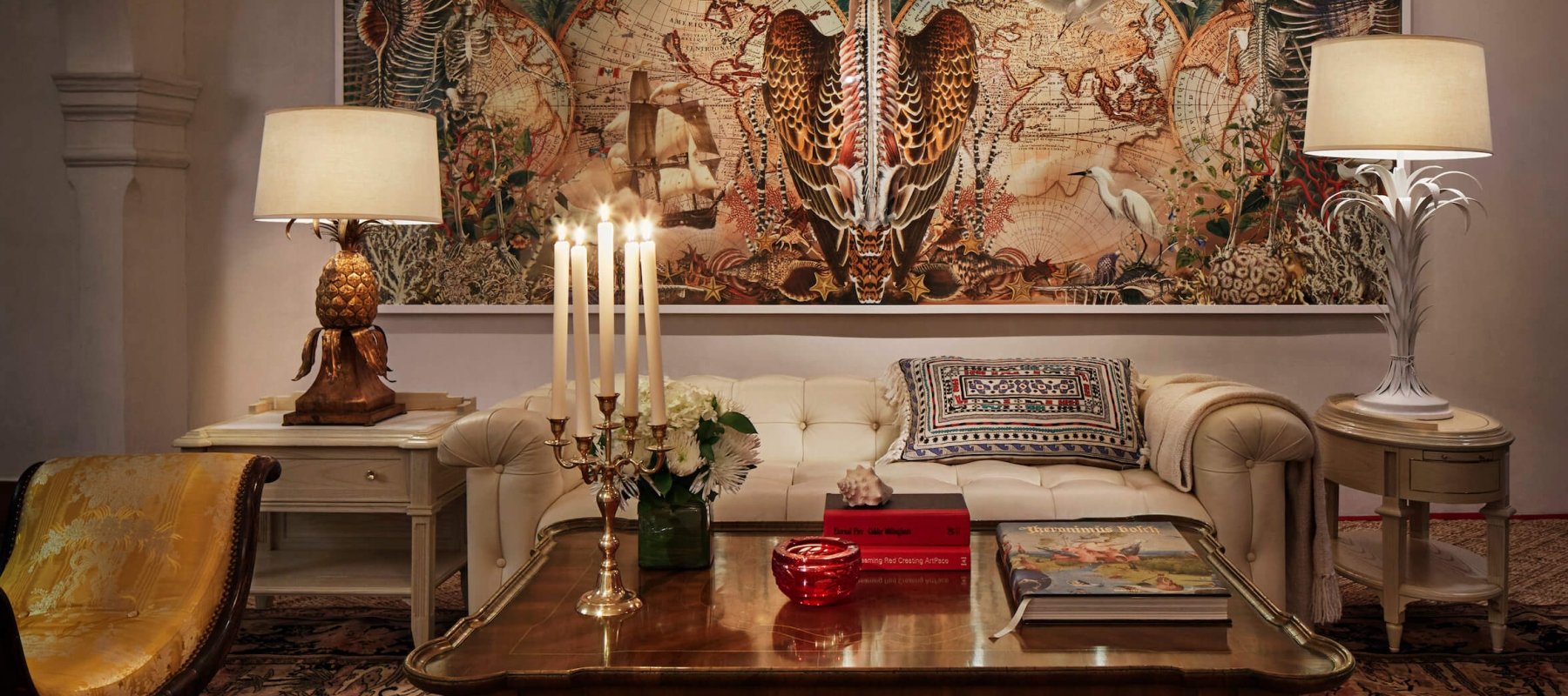 couch and table sit on rug in front of intricate painting and lights