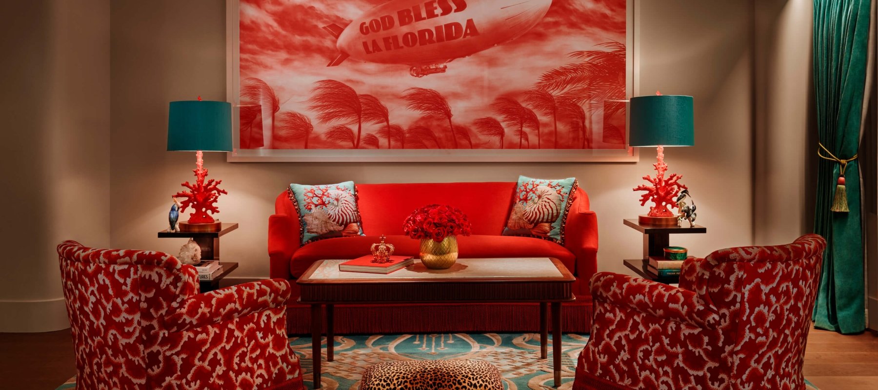 red chairs and couch sit on blue printed rug in front of painting of blimp that reads "God Bless La Florida"