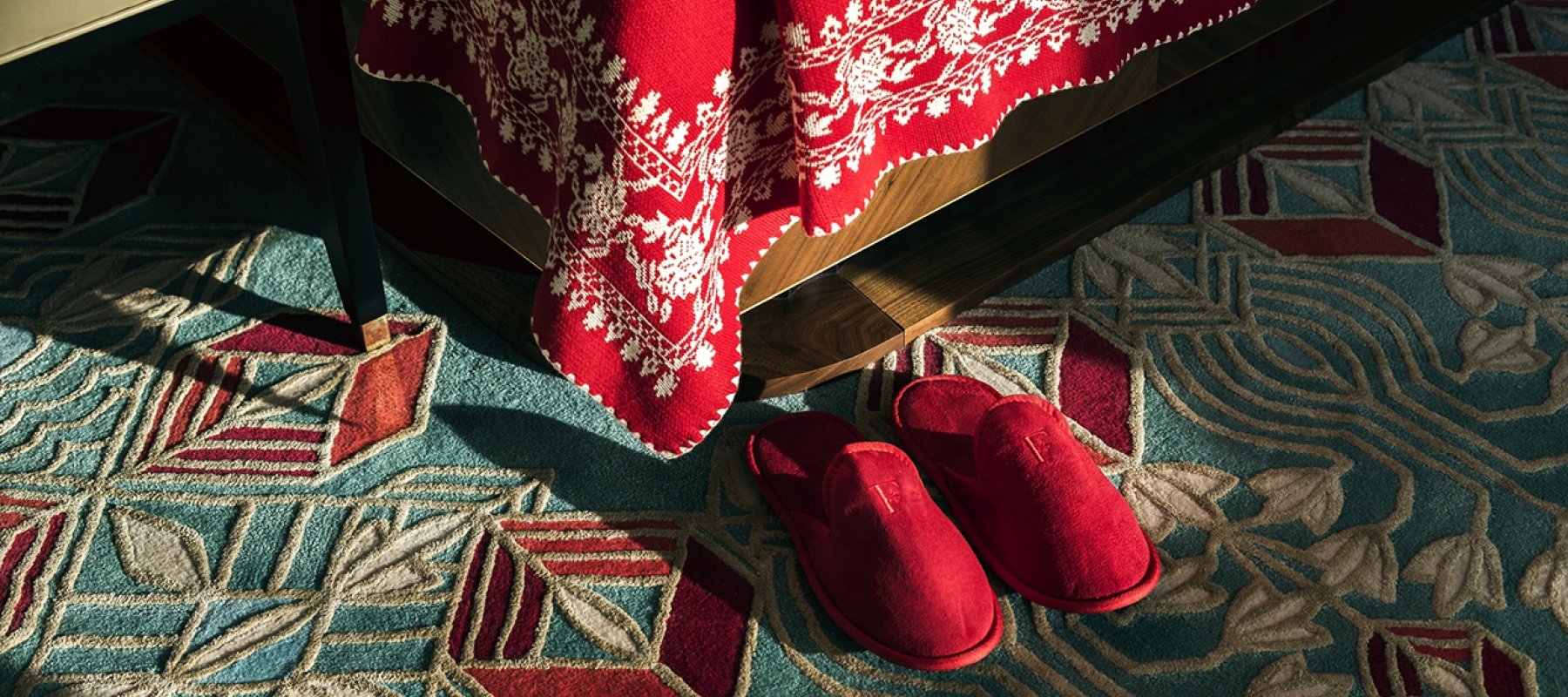 A pair of red slippers on the floor next to a hotel bed