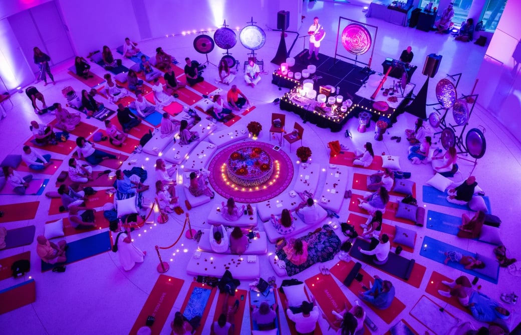 A group of people sitting on yoga mats in a circle with gongs and candles around them.