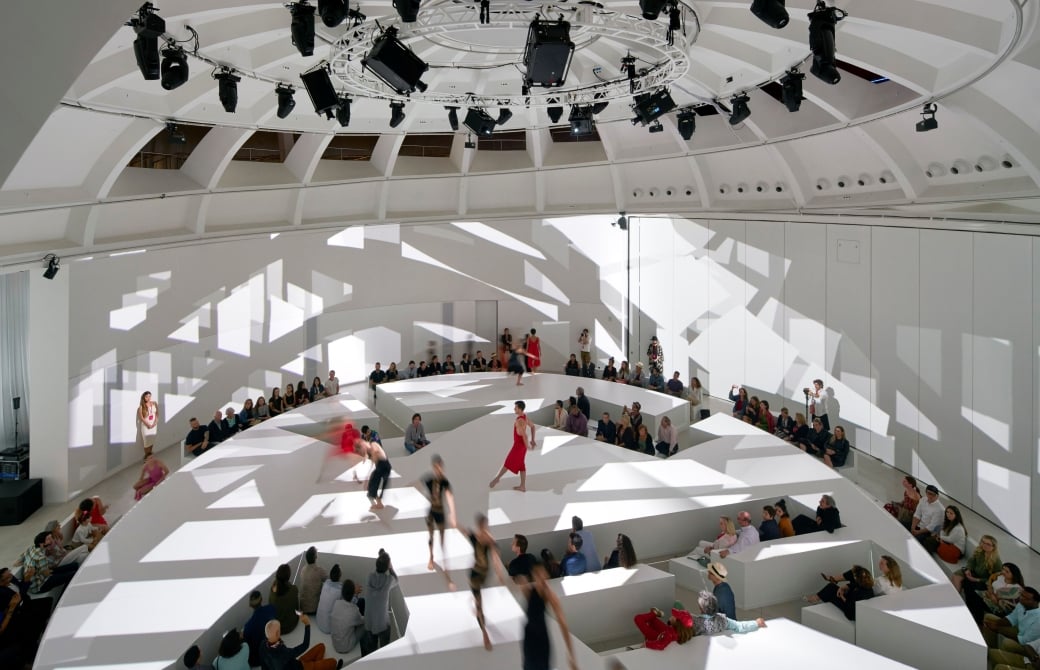 Performance inside the Faena Forum’s circular white hall in Miami Beach, with an audience seated on tiered steps under a ring of stage lights