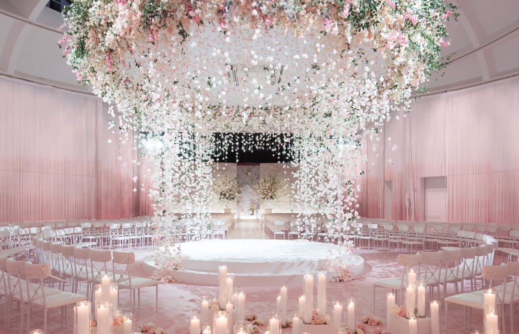 Wedding ceremony at Faena Forum, Miami Beach, with a suspended pink and white floral installation above a circular aisle lined with pillar candles
