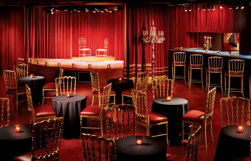 empty lounge area with chairs at multiple tables and a bar along with chairs on stage
