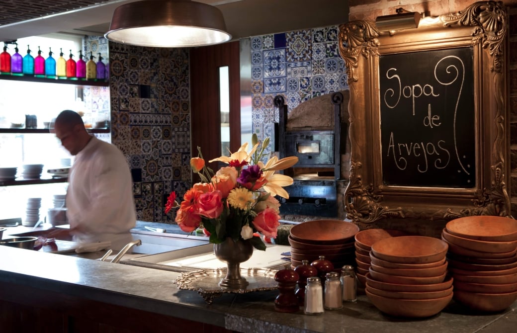 server scoops ladle of food into dish behind bar with flowers and chalkboard sign