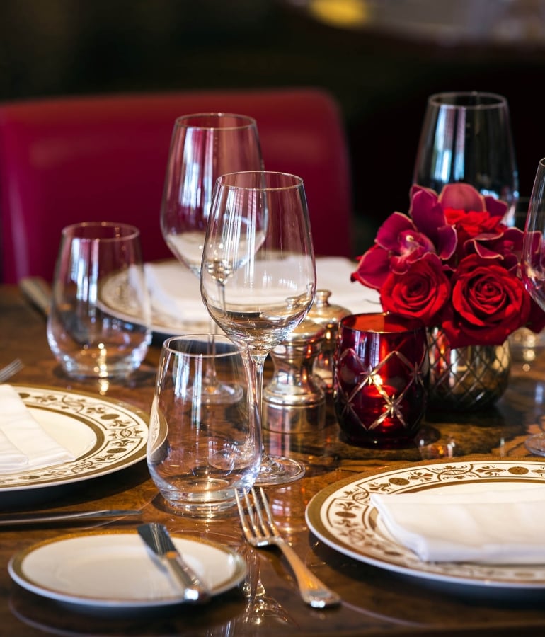A formal dining table set with wine glasses, plates, and red roses.