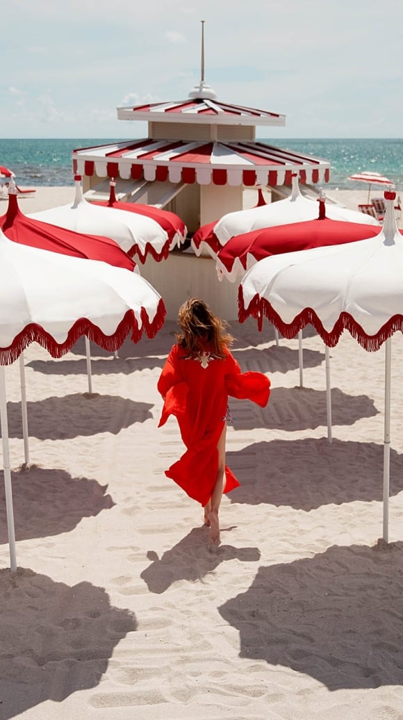 A woman in a red dress walking on the beach with red and white umbrellas