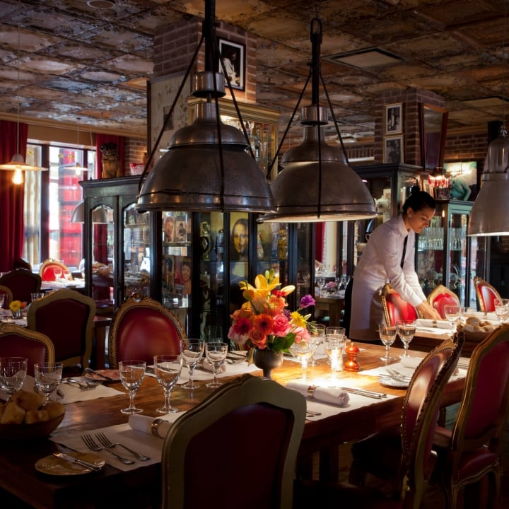 server sets table in room with tin ceiling, large light fixtures, and red chairs framed in gold