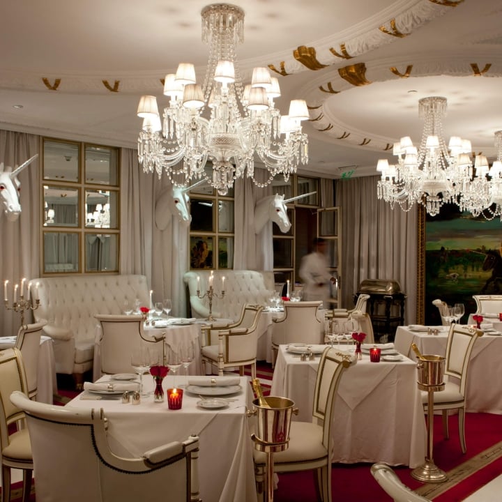 grand dining room with three chandeliers, unicorn heads on walls, red carpet, and white booths, tables, and chairs