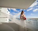bride stands on balcony with veil flowing in the wind