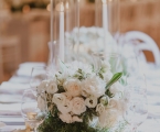 White floral arrangement with tall glass incased candles as center pieces on white table
