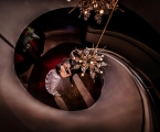 bride and groom stand at bottom of spiral staircase with chandelier hanging above them