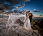 bride and groom kiss on rocks beside the ocean