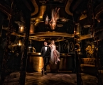 bride and groom sit on a bar in dimly lit room with a golden hue