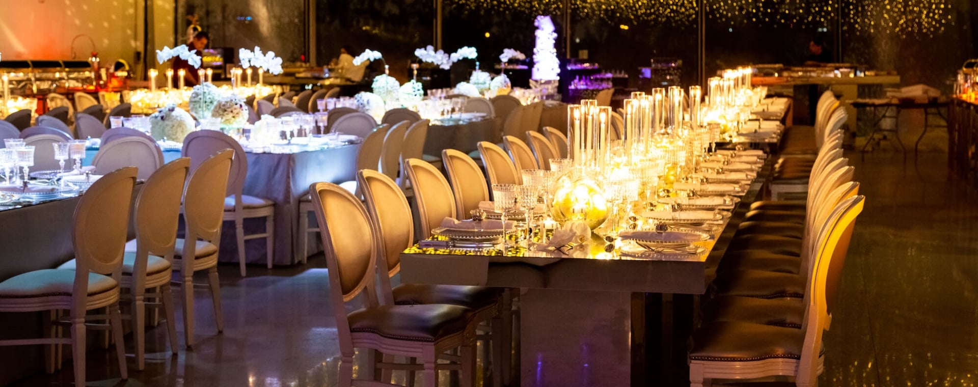 A long table set for a formal dinner with white chairs, candles, and flowers.