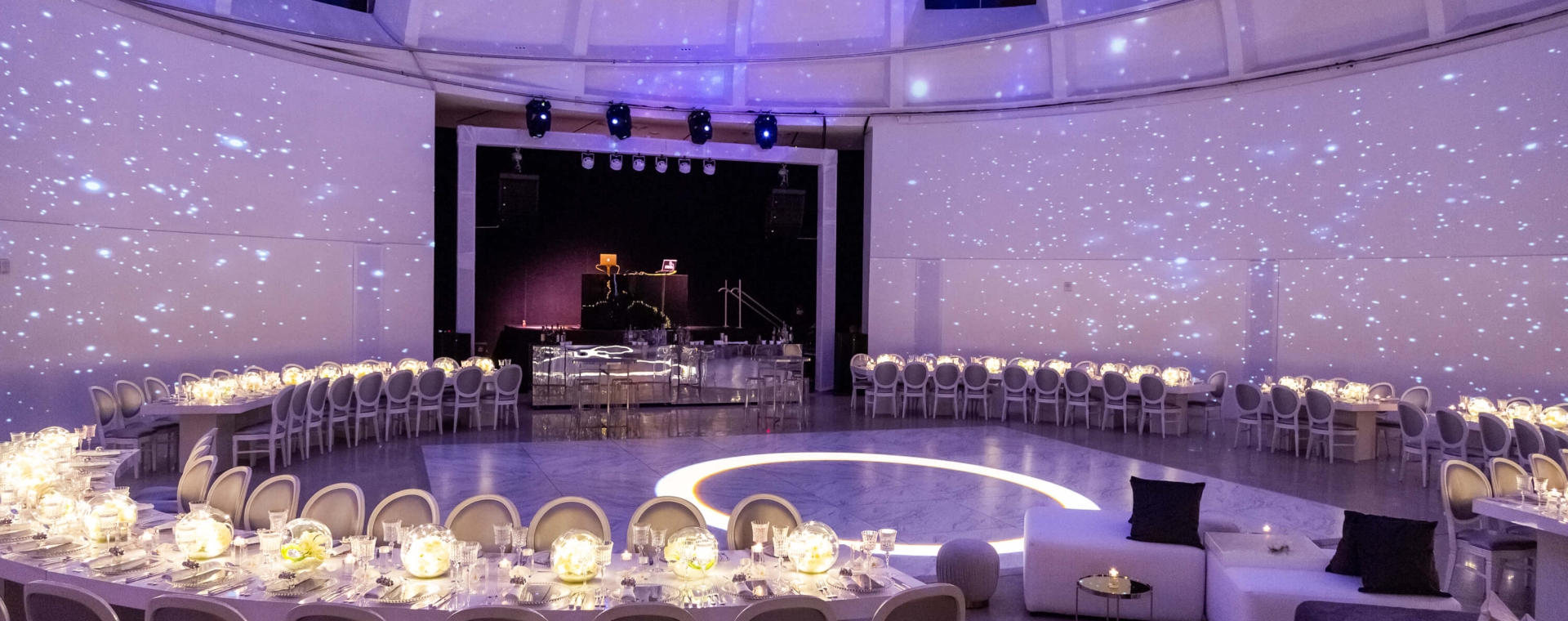 A large, circular dining room with tables set for a meal, a stage in the background, and a starry ceiling.