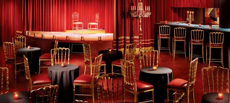 empty lounge area with chairs at multiple tables and a bar along with chairs on stage