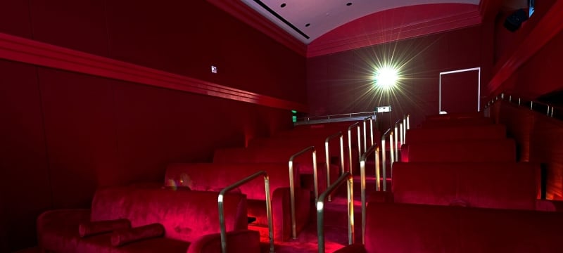 red velvet stairs and movie-theatre style seating with gold handrail with light from projector in background