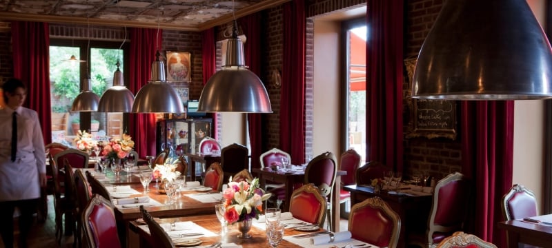 server walks alongside table in room with tin ceiling, large light fixtures, and red chairs framed in gold