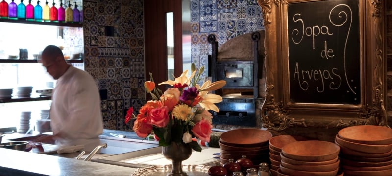 server scoops ladle of food into dish behind bar with flowers and chalkboard sign