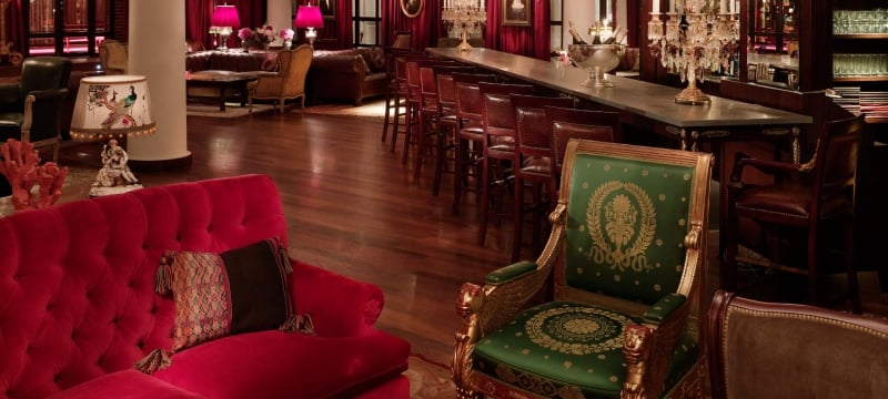 green chair and red couch sit in bar area with red curtains and chandeliers