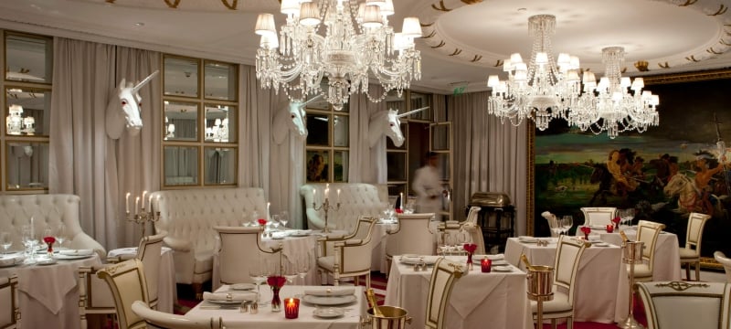 grand dining room with three chandeliers, unicorn heads on walls, red carpet, and white booths, tables, and chairs