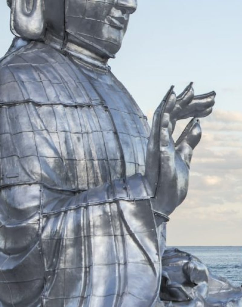 buddha statue with hand lifted sits in front of ocean
