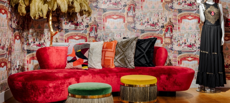 Mannequin in a vintage black dress next to a long red velvet couch 