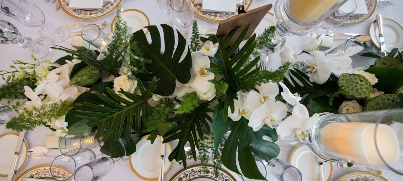 gold and white table placement with monstera leaves and white orchid centre piece