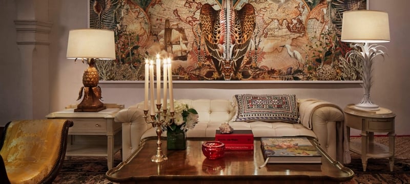 couch and table sit on rug in front of intricate painting and lights