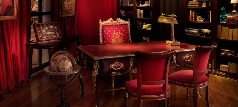red chairs sit at desk with gold lamp and globe beside shelves full of books