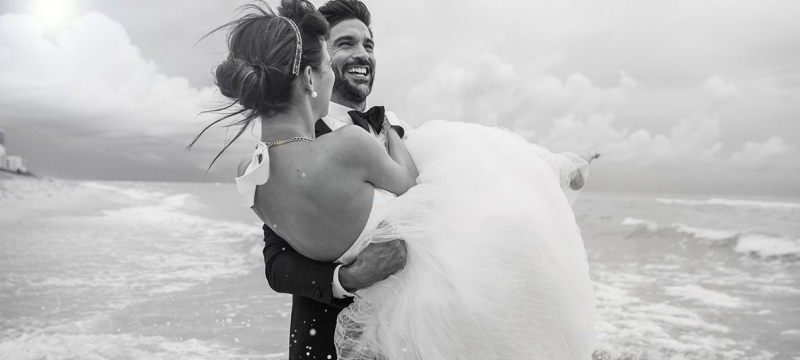 groom carries bride on the beach