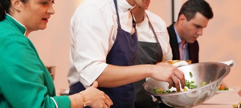 group of cooks work to prep dozens of plates of food sitting on table in front of them