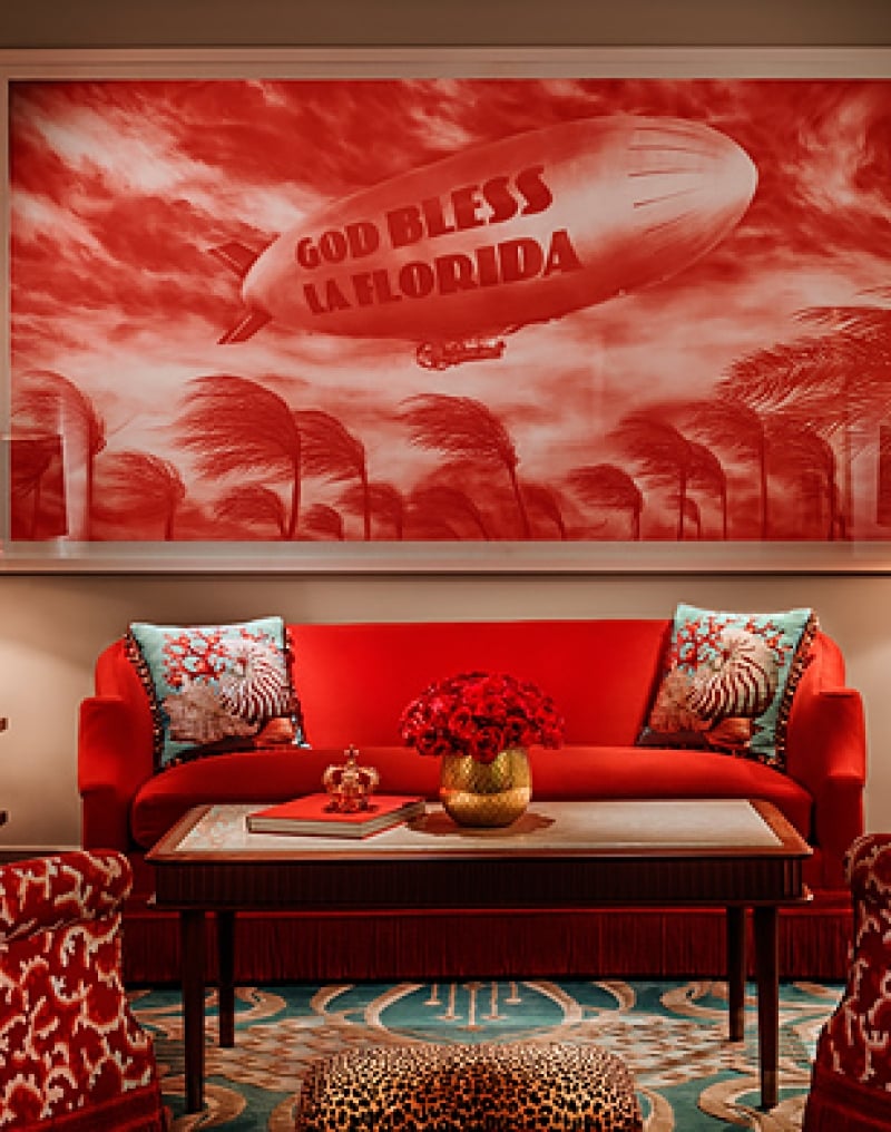 red couch sits between two teal lamps with a God Bless La Florida hung on the wall