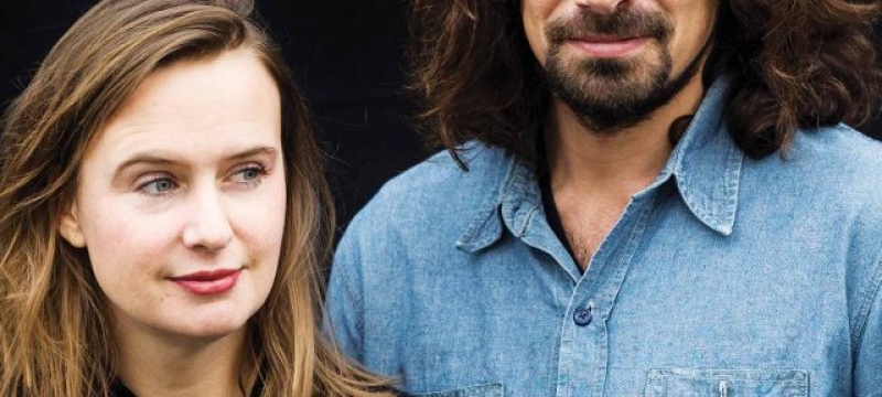 blonde haired woman and dark haired & bearded man stand side by side