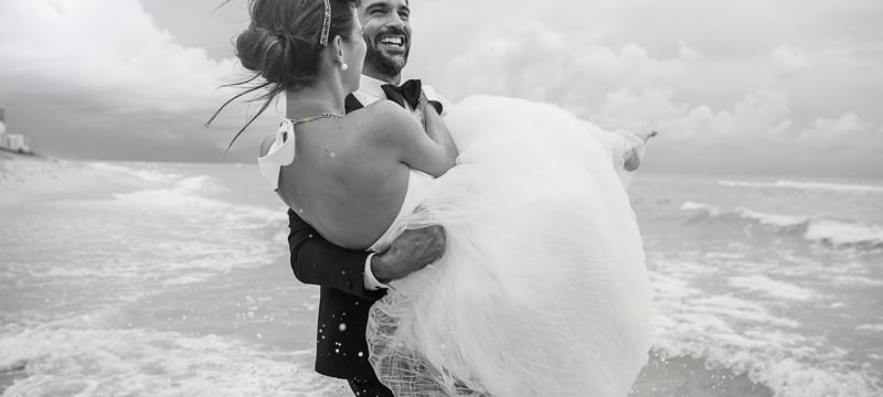 groom carries bride along the oceanfront
